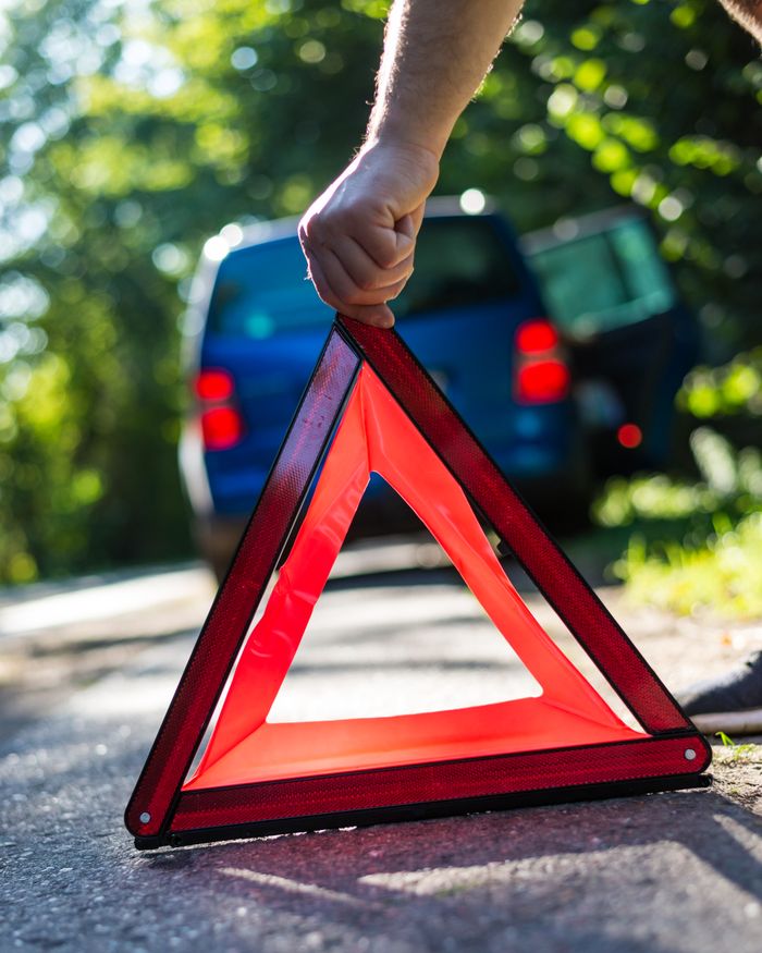 About Close-up of a hand placing an emergency warning triangle by a car.